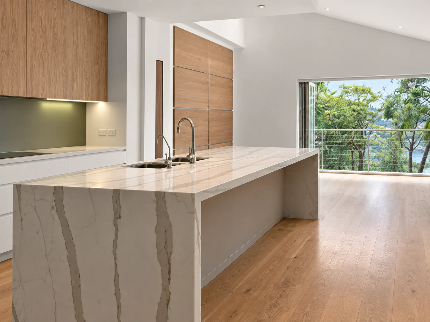 Oak kitchen with a veined stone waterfall island and garden views