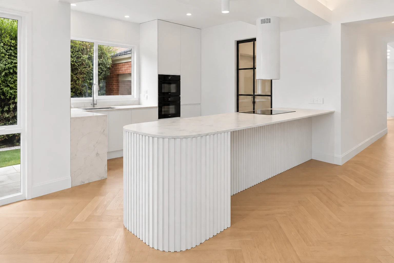 White kitchen with a long rounded fluted island and herringbone flooring