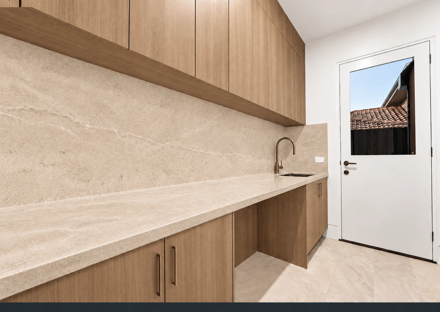 Smoked oak laundry cabinetry with a warm beige stone worktop and splashback