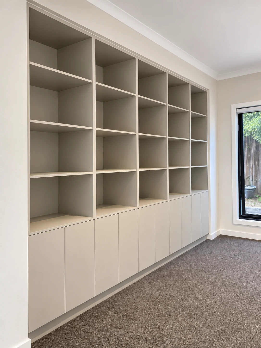 Full-height warm grey bookcase with open shelves and handleless storage doors