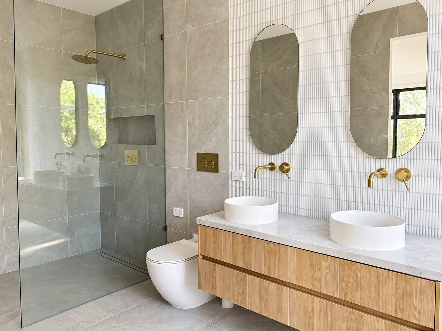 Oak double vanity with round vessel basins, oval mirrors and brass taps