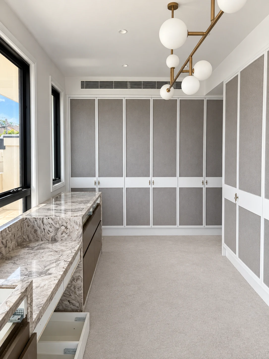Bright dressing room with grey-panel wardrobes, brass handles and a stone dressing bench
