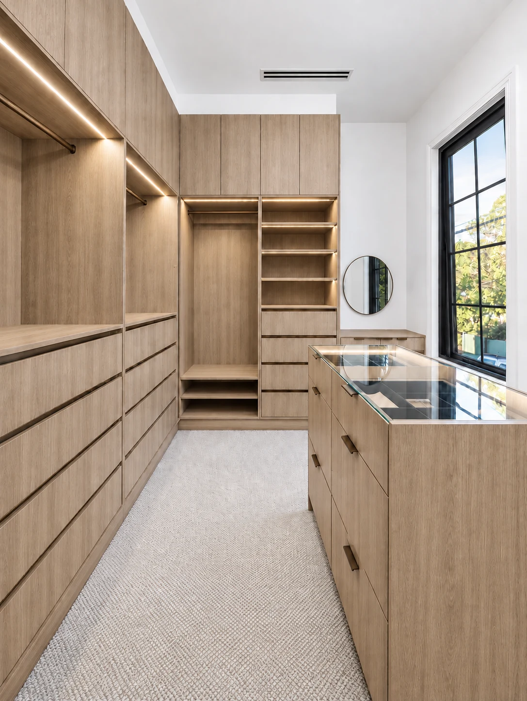 Natural oak walk-in wardrobe with dark bronze handles, illuminated shelving and a glass-top island